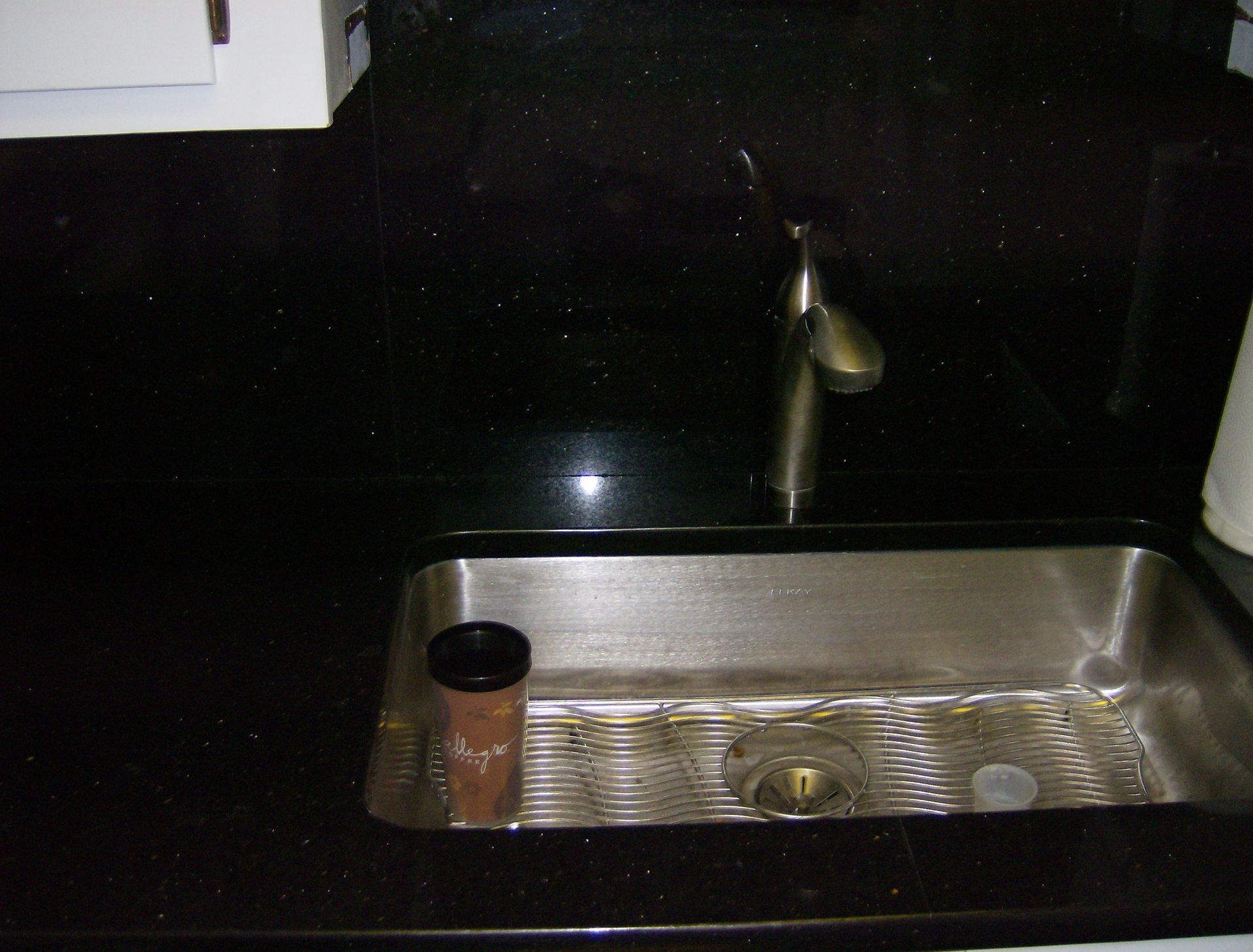 Stainless steel kitchen sink with faucet on black countertop.