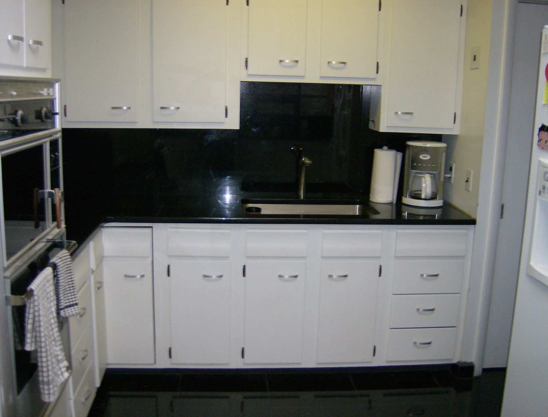 White kitchen cabinets with black backsplash and countertops; sink, appliances visible.