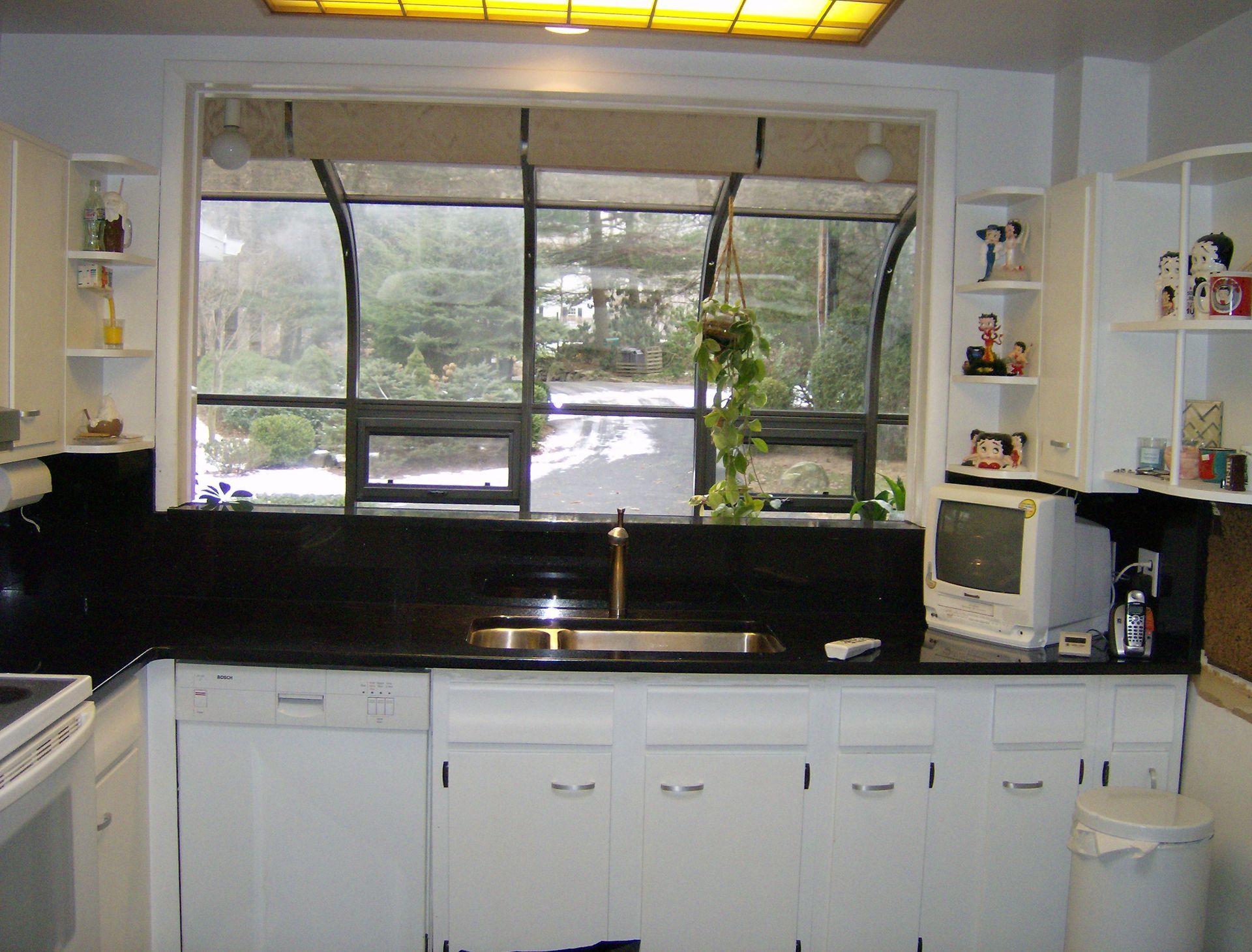 White kitchen with black countertops, window with trees, and a retro computer.