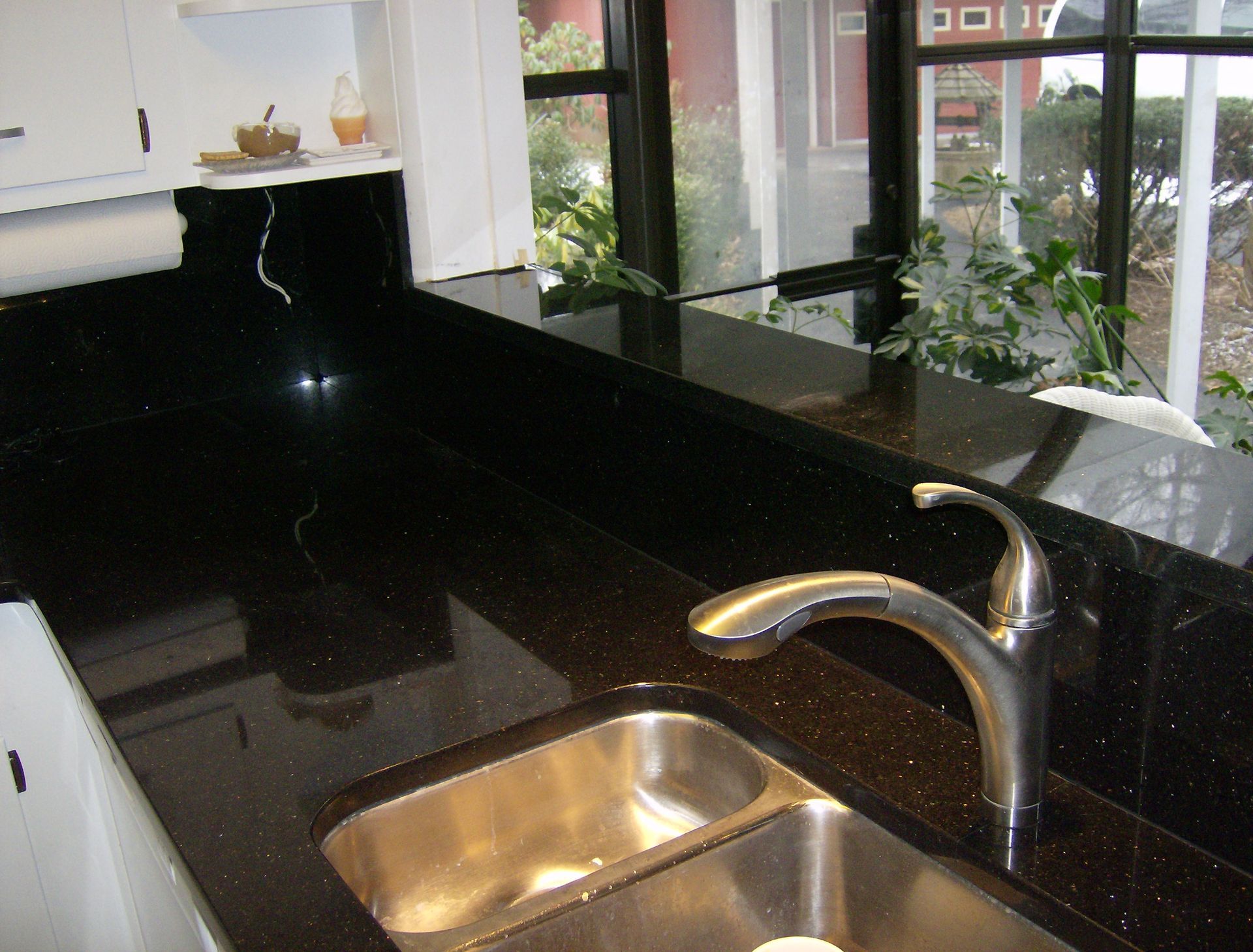 Kitchen counter with stainless steel sink and faucet; dark countertop near window.