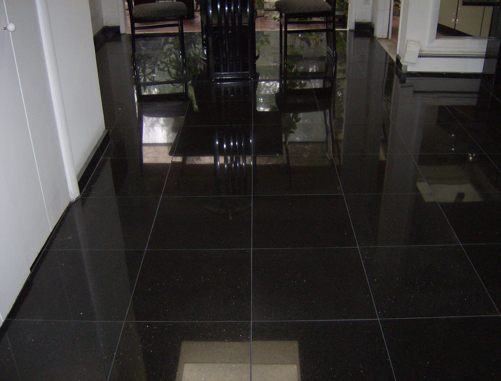 Black, glossy tiled floor reflects a dining area with chairs.