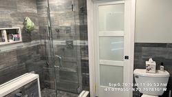 Bathroom with gray tiled shower, glass door, white door, and a toilet.