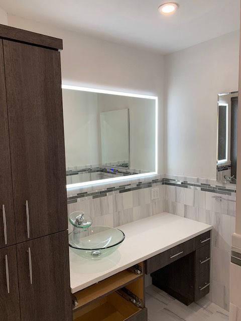 Modern bathroom with a glass bowl sink, large illuminated mirror, and dark wood vanity.