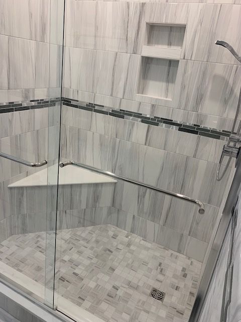 Shower with gray and white tile, glass door, built-in seat, and recessed shelf.