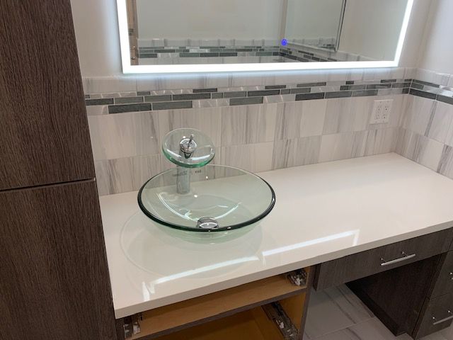 Bathroom vanity with a glass bowl sink, white countertop, and illuminated mirror.