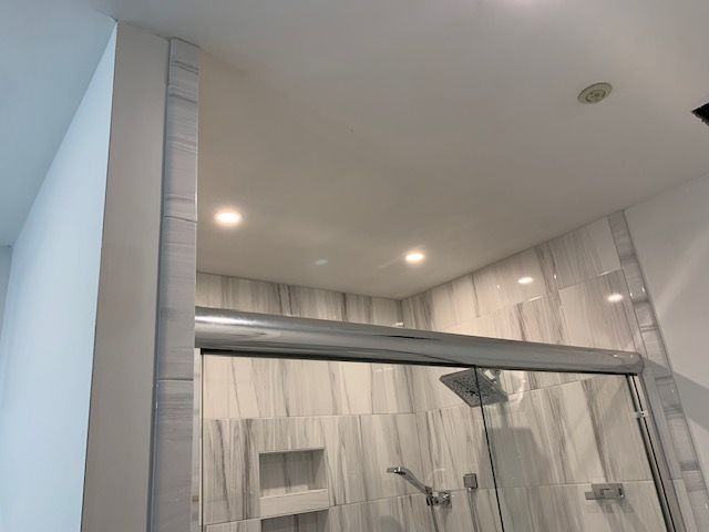 White tiled shower with glass door, chrome fixtures, recessed lighting.
