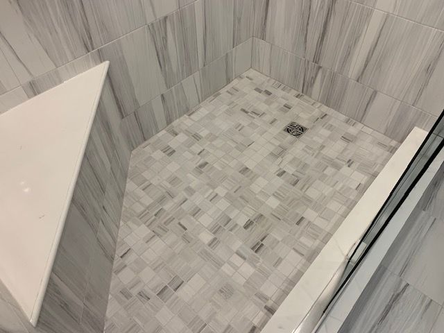 A tiled shower with a corner seat, and a glass door. The floor has a mosaic pattern.