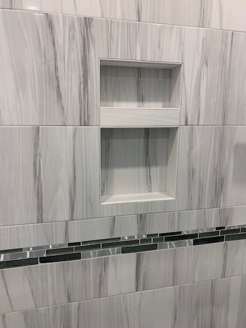 Shower with built-in shelf, featuring white and gray marble-look tiles and a dark mosaic accent strip.