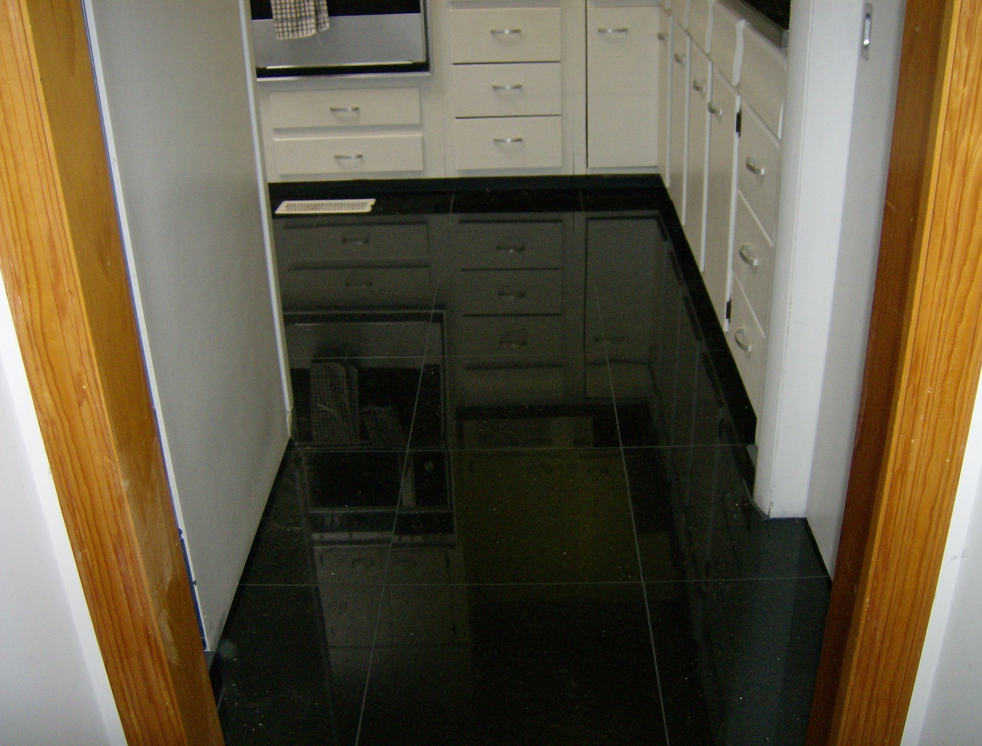 Black tiled kitchen floor reflecting white cabinets.