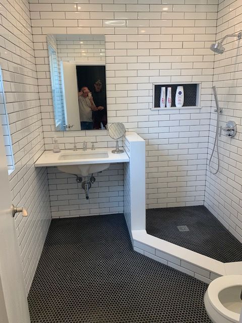 White-tiled bathroom with a walk-in shower, pedestal sink, and dark tile floor.