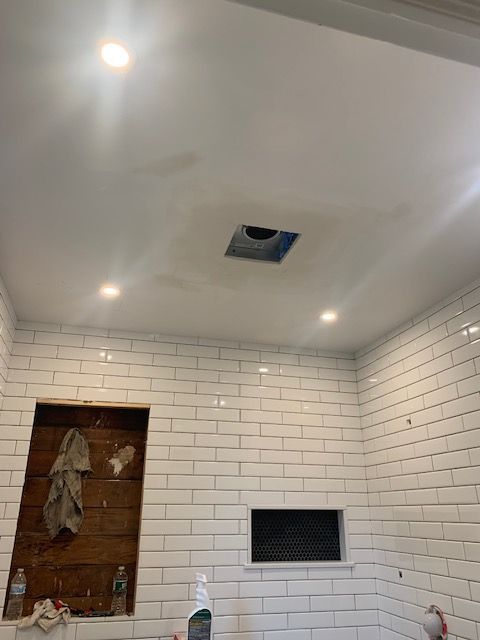 White tiled bathroom with a ceiling fan opening, recessed lighting, and a wooden niche in the wall.