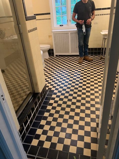 Bathroom with black and white checkered floor, black tiled border, and a person holding a mask.