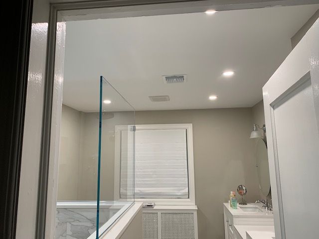 Bathroom interior viewed through a doorway. Includes a shower, sink, and window with blinds; neutral color scheme.
