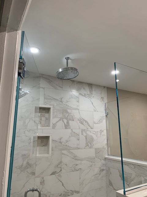 Shower with marble-look tile, glass walls, and rain shower head. Two recessed niches.