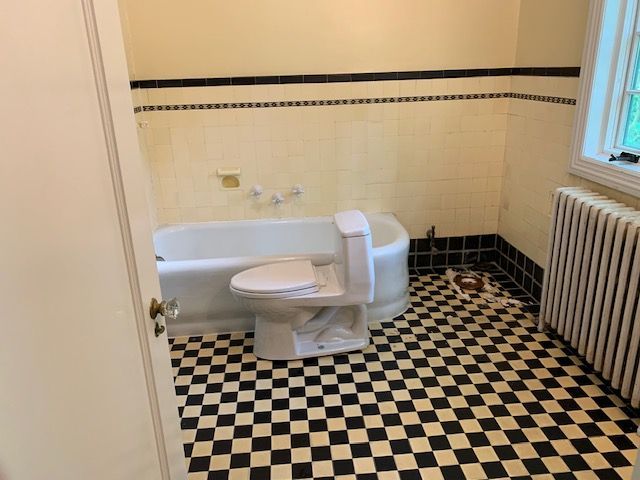 Bathroom with black and white checkered floor, white bathtub, and toilet, and black trim.
