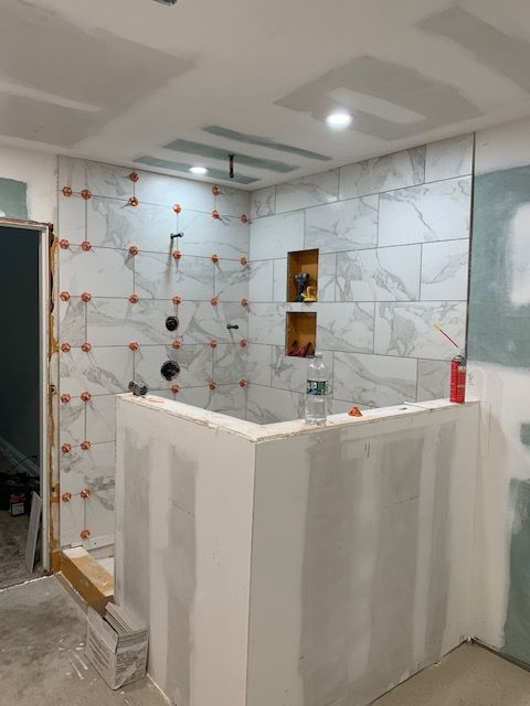 Bathroom under construction; tiled shower with tile leveling system, drywall and fixtures visible.