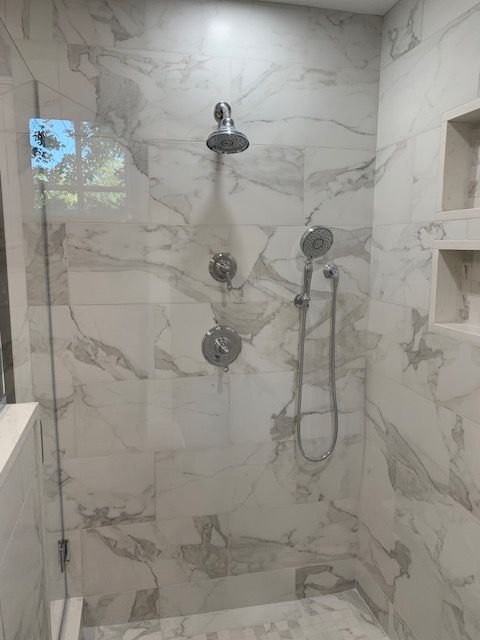 Shower with marble-look tile, multiple showerheads, and built-in shelving.