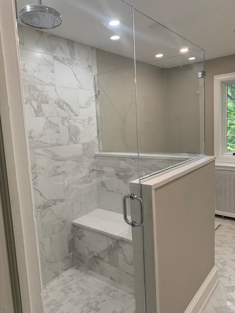 Modern shower with marble-look tile, glass enclosure, built-in bench, and chrome hardware.