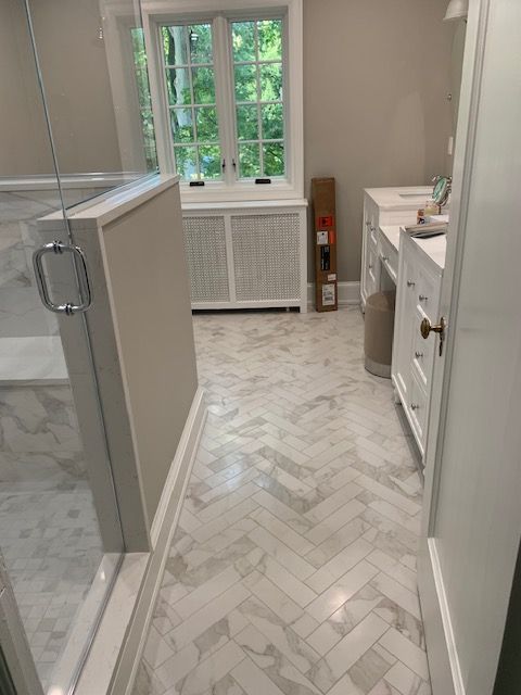 Bathroom with white herringbone tile floor, shower, window, and vanity.