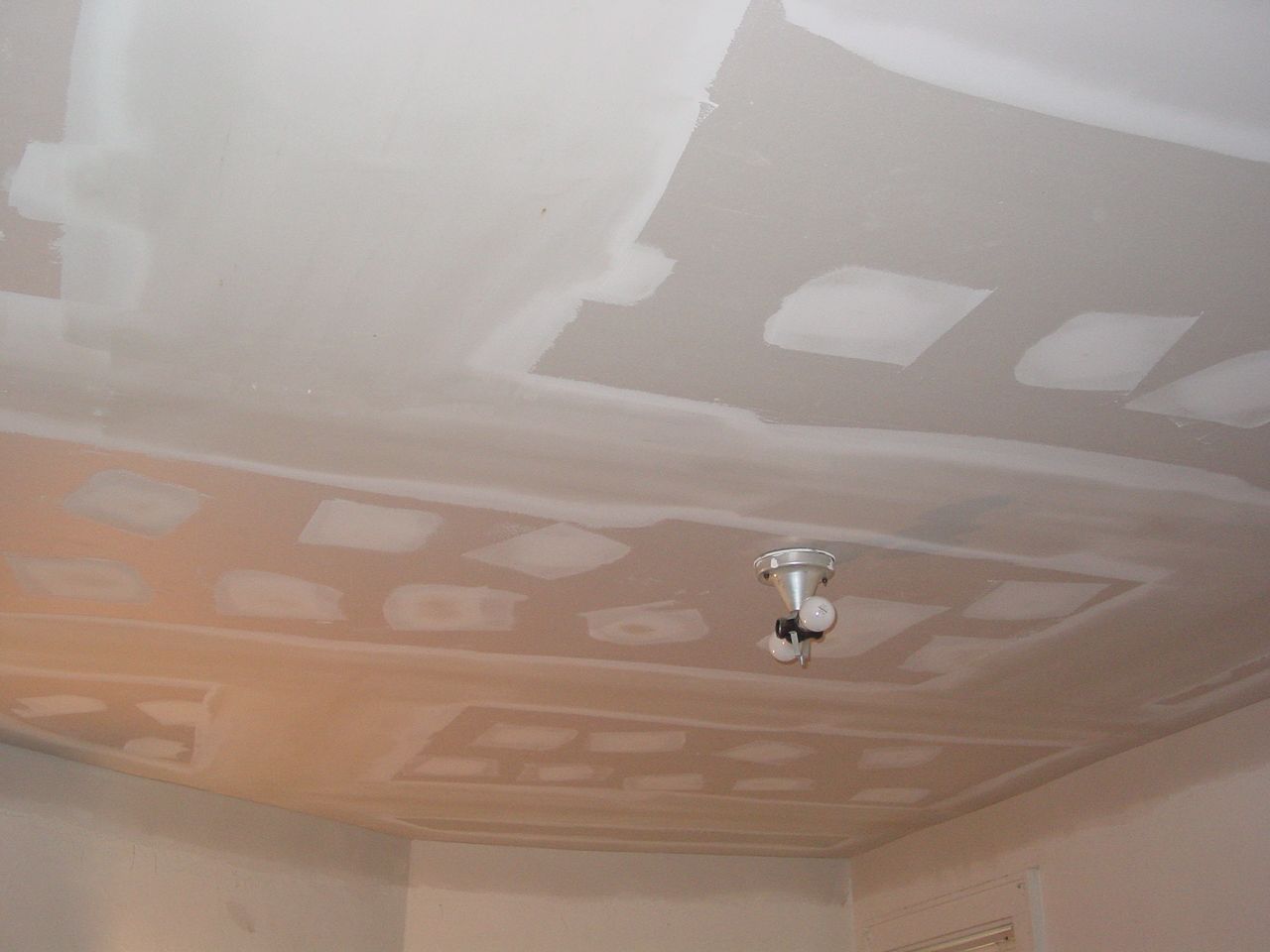 White drywall ceiling with patches of compound, recessed section, and a sprinkler head.