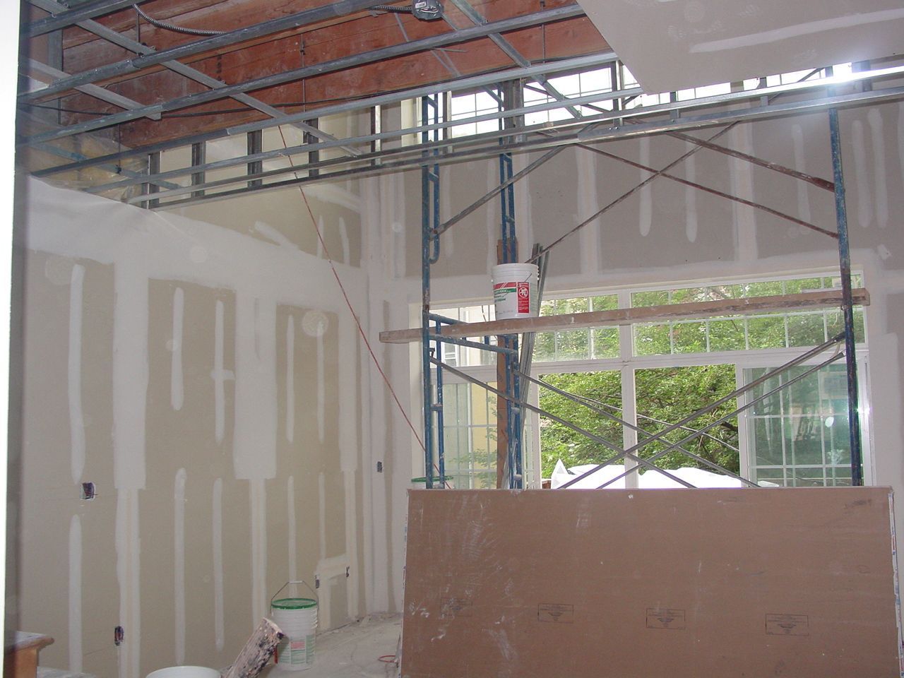Construction site: drywall installation; scaffolding near window, exposed metal framing.