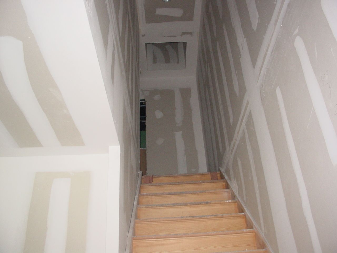Staircase under construction, drywall-lined walls, wooden steps, view from below, neutral colors.