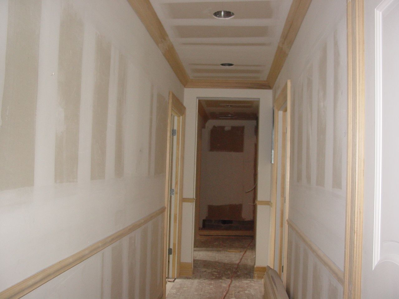 Hallway under construction with unfinished walls, wood trim, and open doorways.