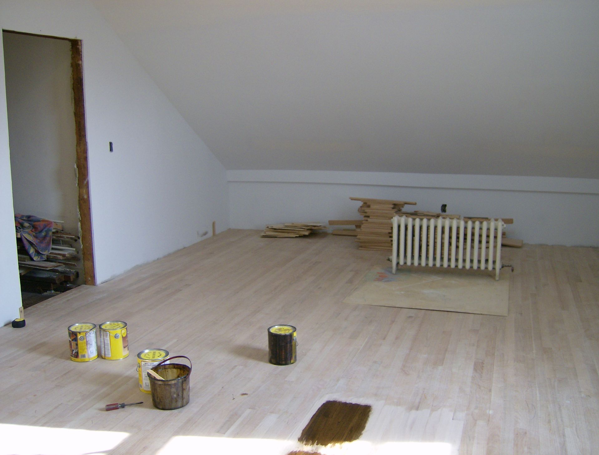 Bare wooden floor in room being renovated, paint cans and radiator present.