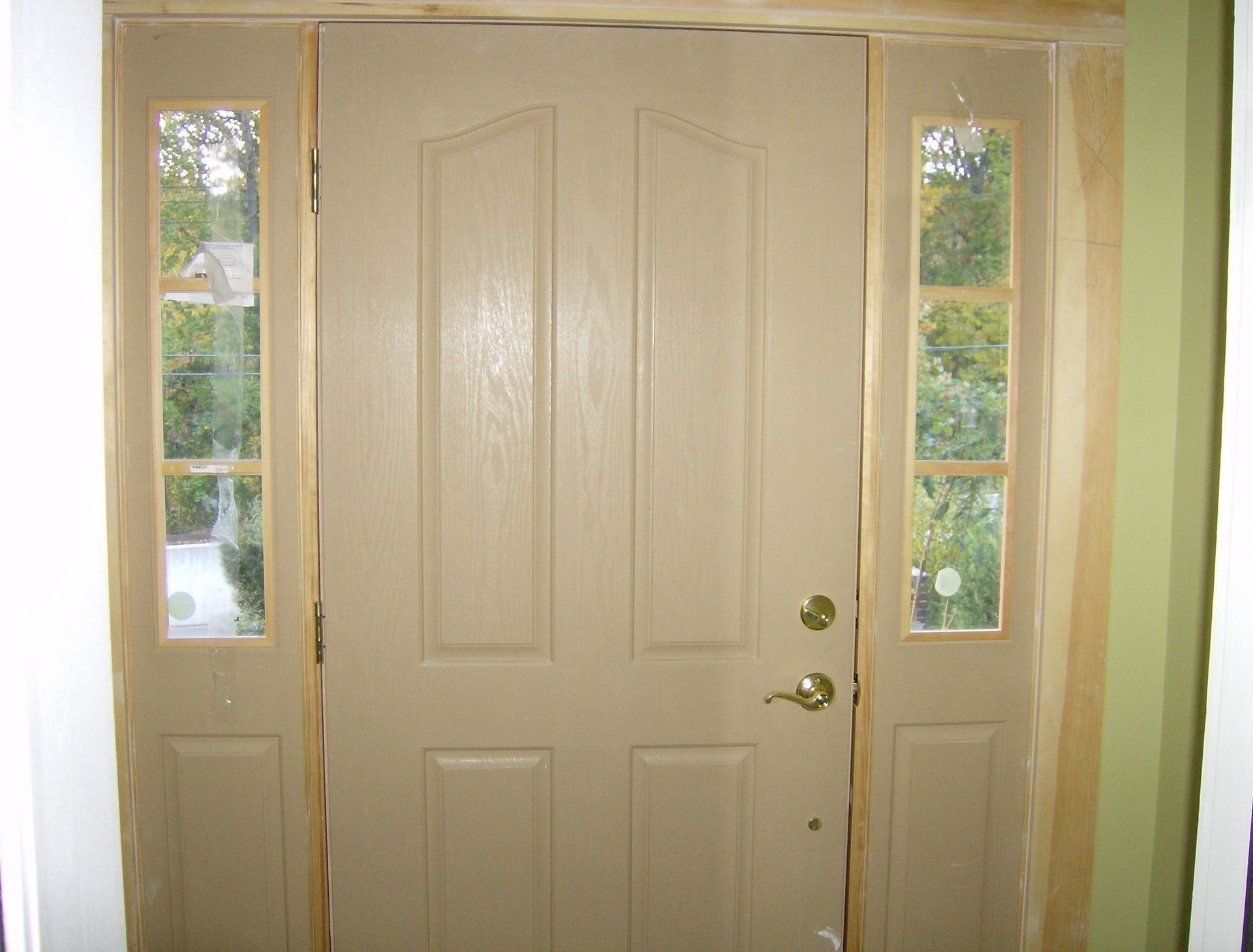 Beige front door with sidelights, viewed from inside a house. Wooden frame.