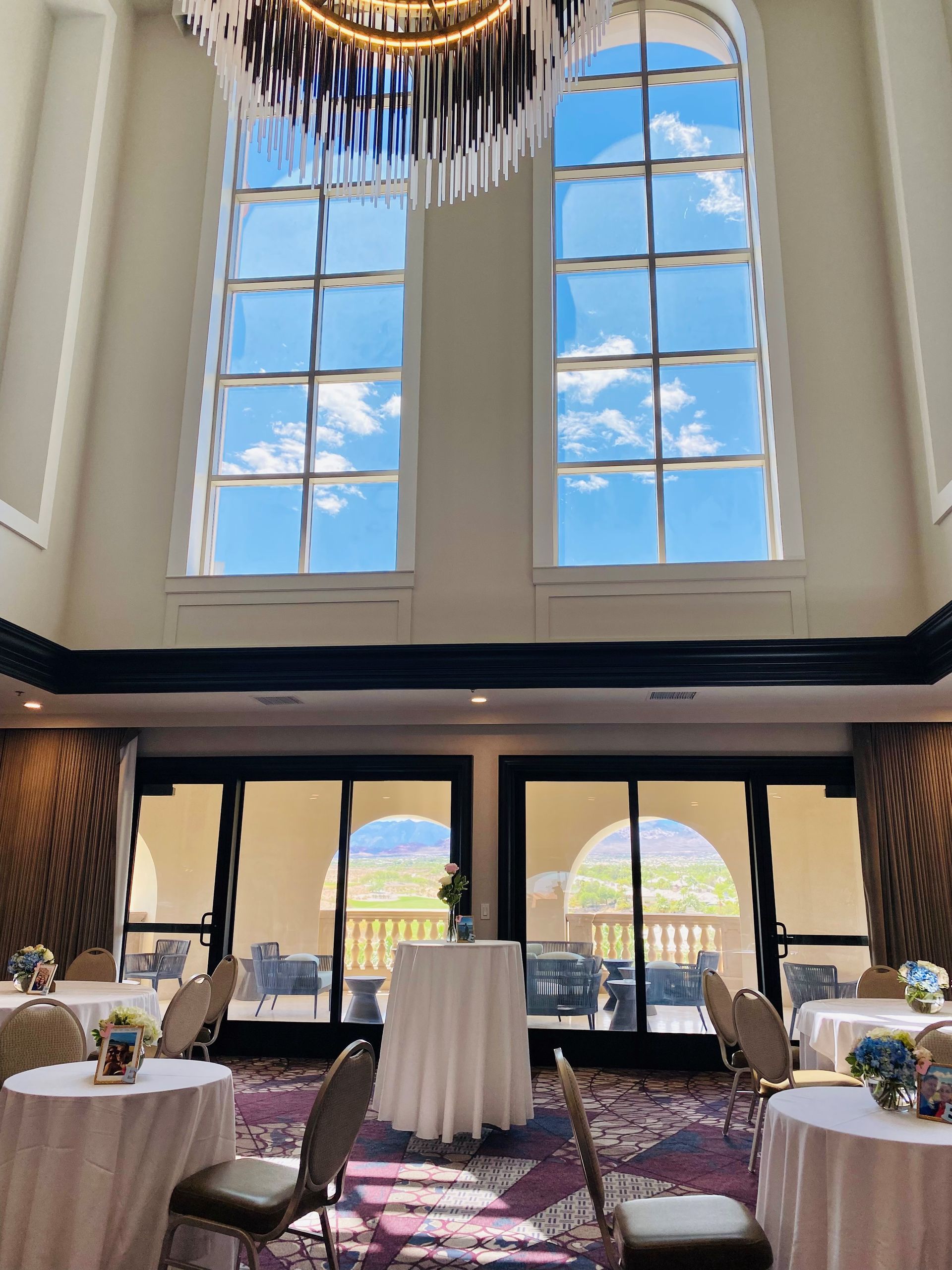Interior of a room with tall arched windows showing a blue sky. Tables are set for an event.