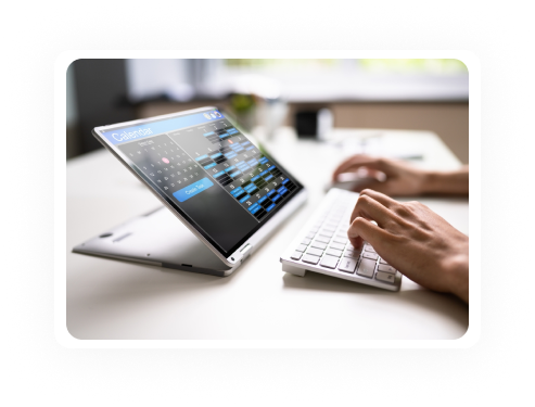 Person using a laptop with a calendar displayed, typing on a separate keyboard at a desk.