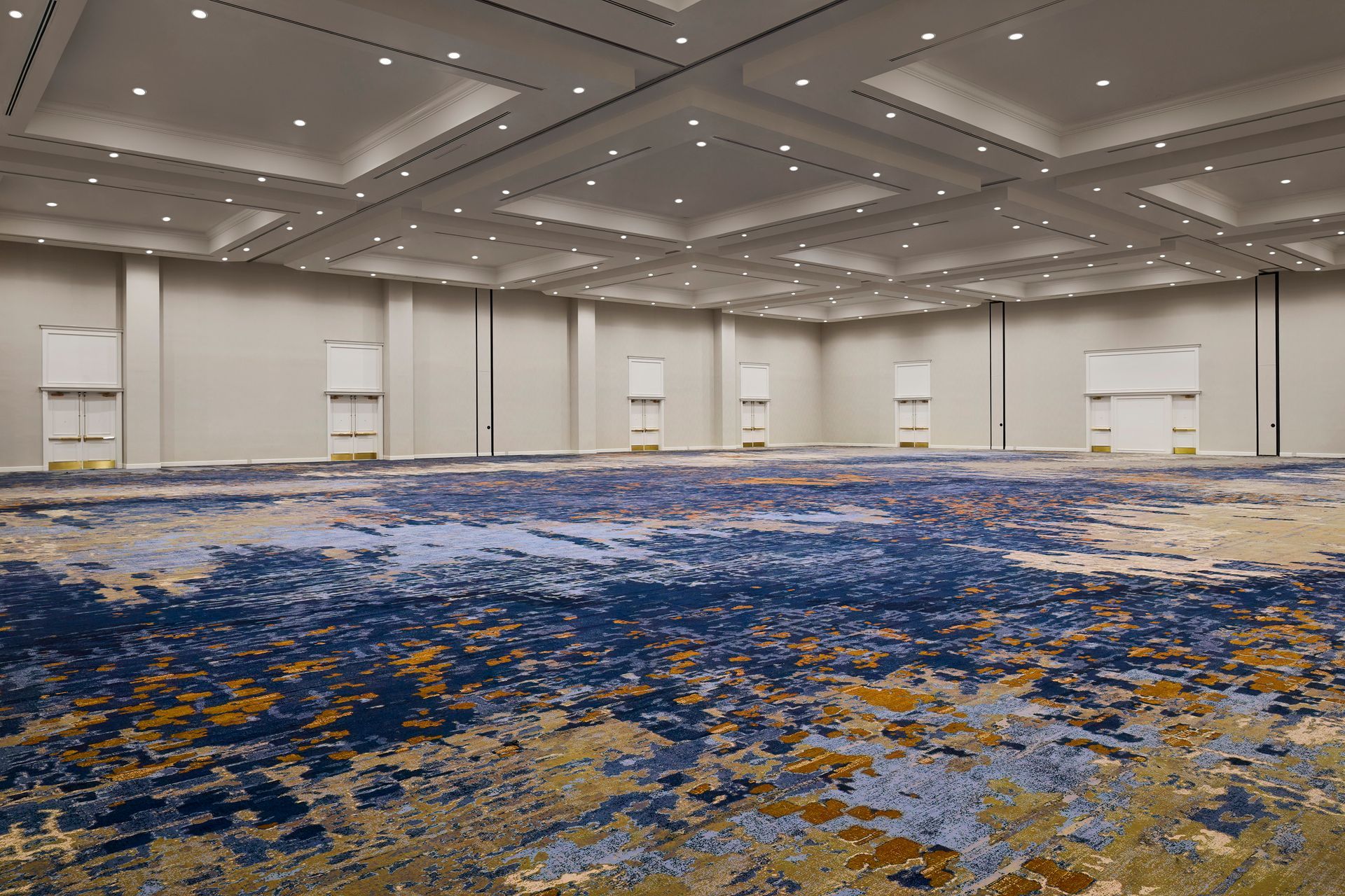 Empty, large event space with a patterned blue, tan, and gold carpet, and light-colored walls and ceiling.