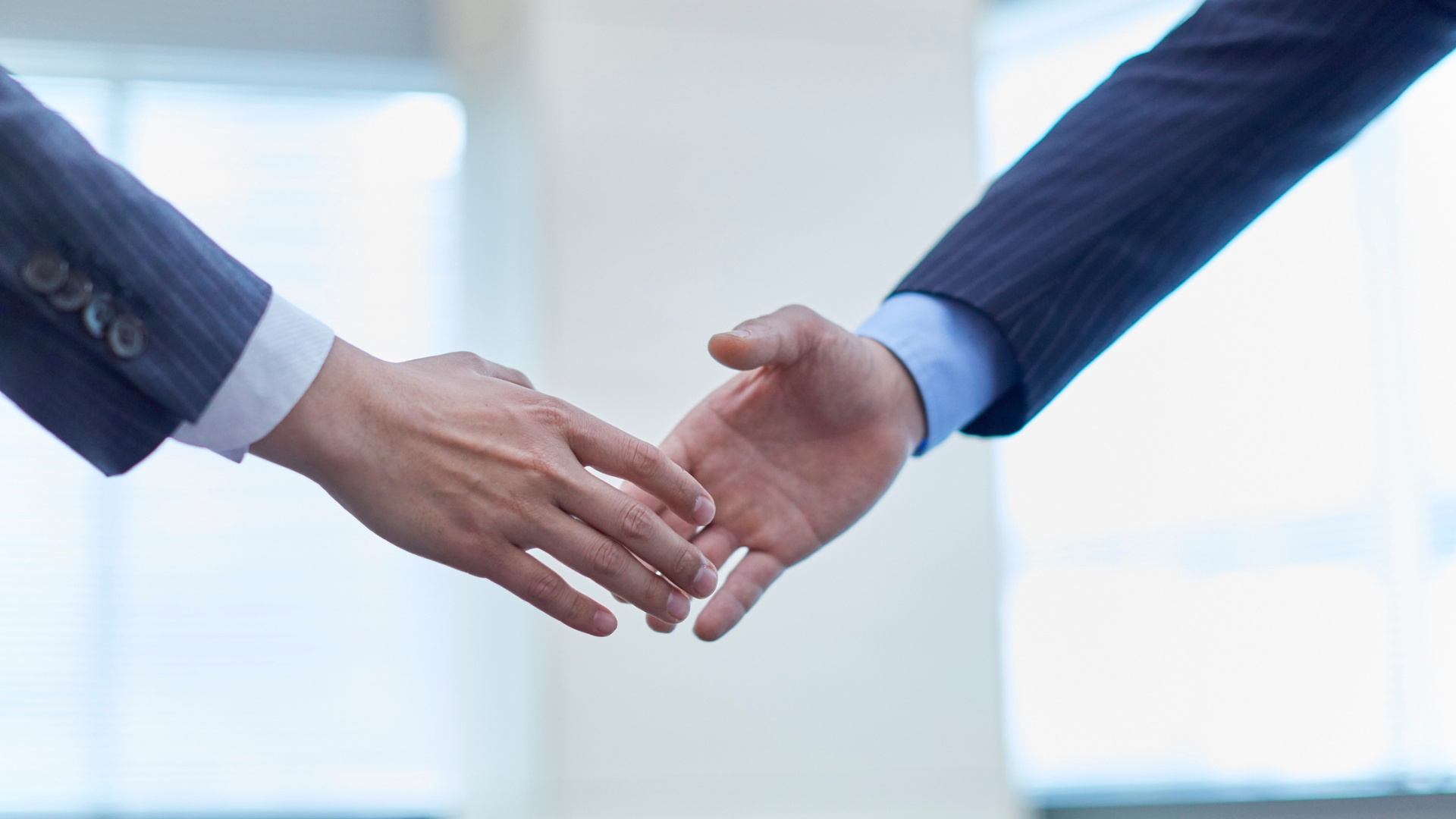 Two businessmen are shaking hands in front of a window.