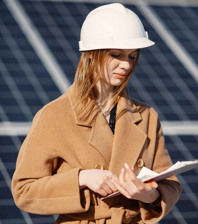 Woman in hard hat and coat reviewing documents in front of solar panels.