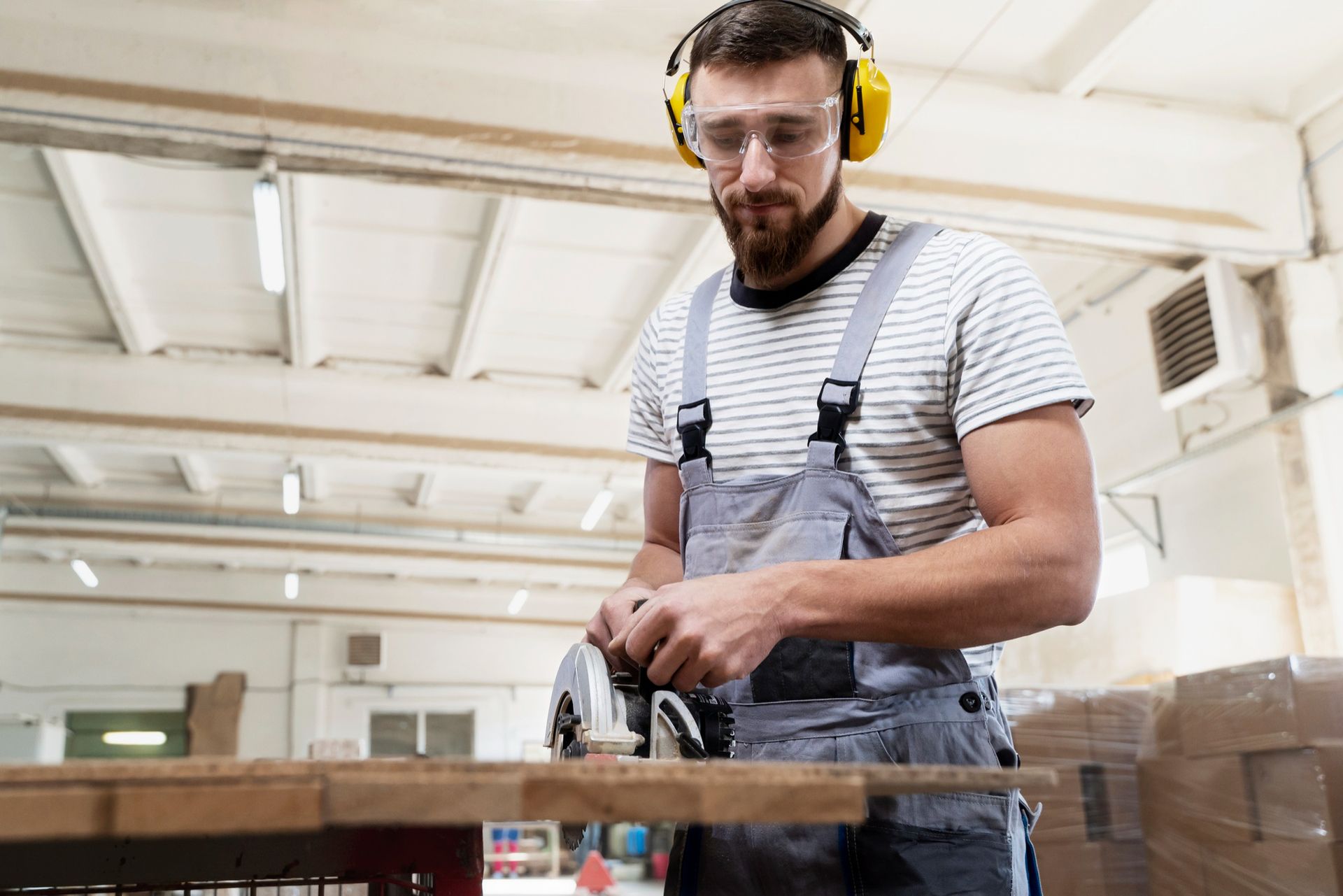 Man in safety gear, using a power tool to cut wood in a workshop.