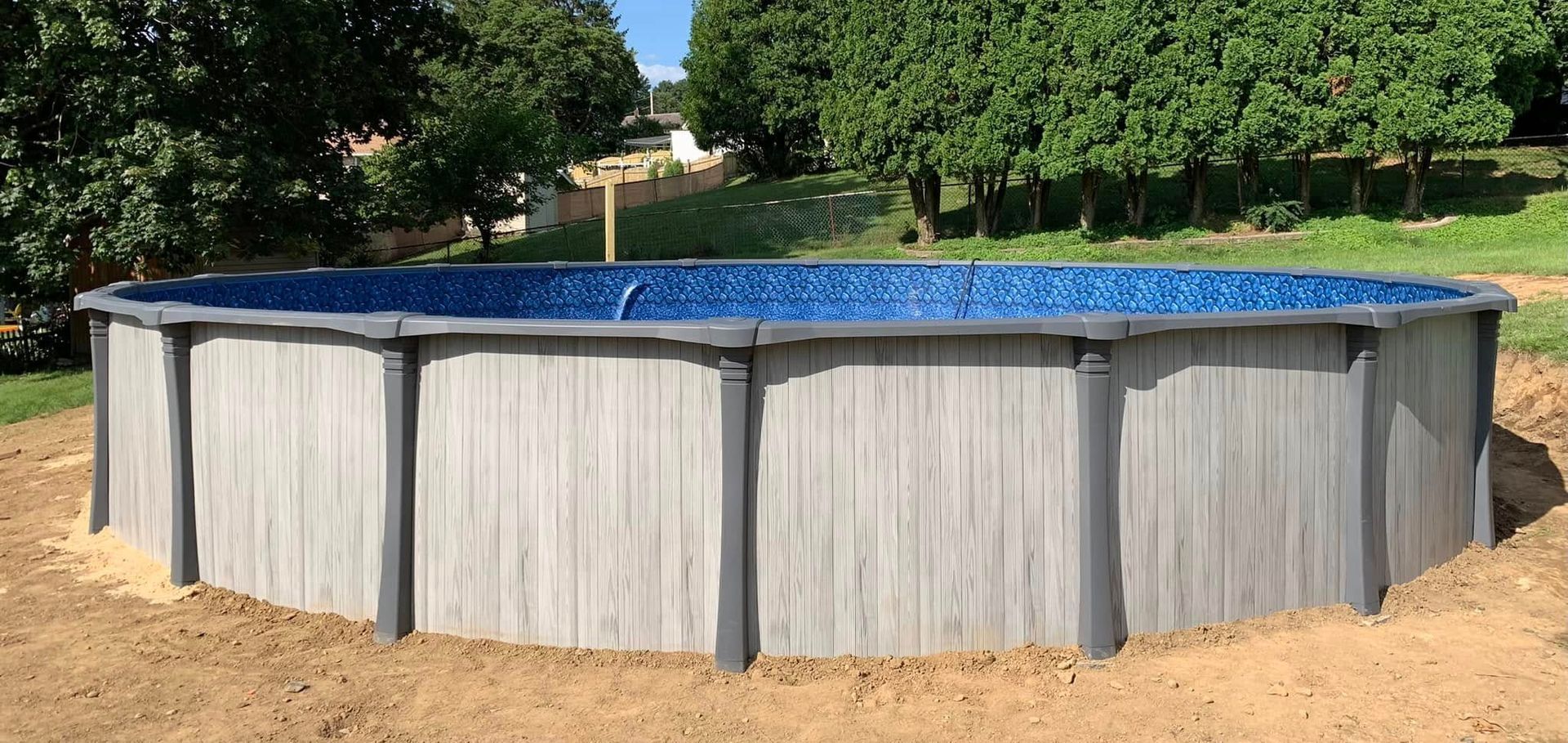 A large swimming pool is sitting in the middle of a dirt field.