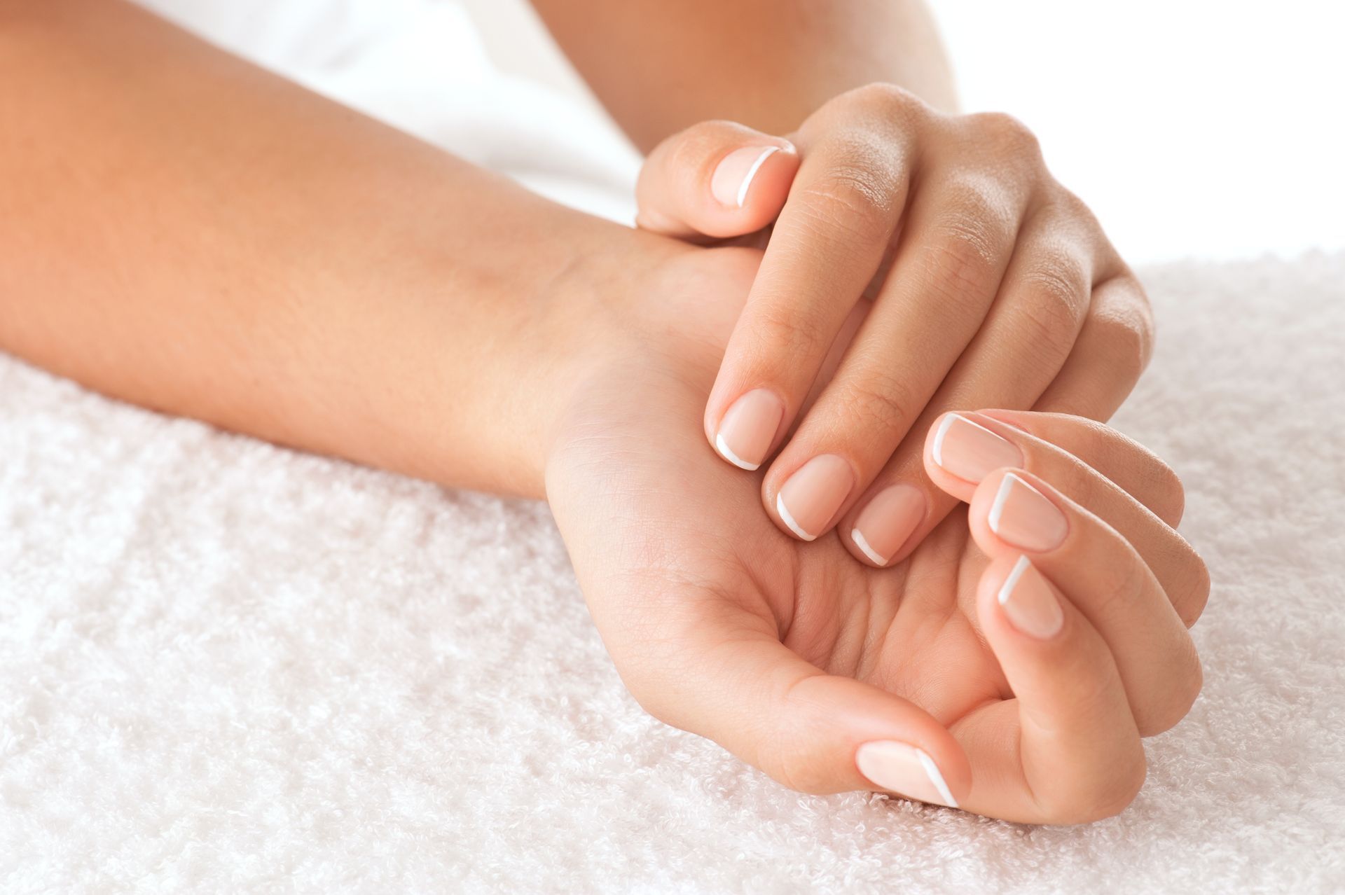 Hands resting on a white towel, fingernails with white tips.