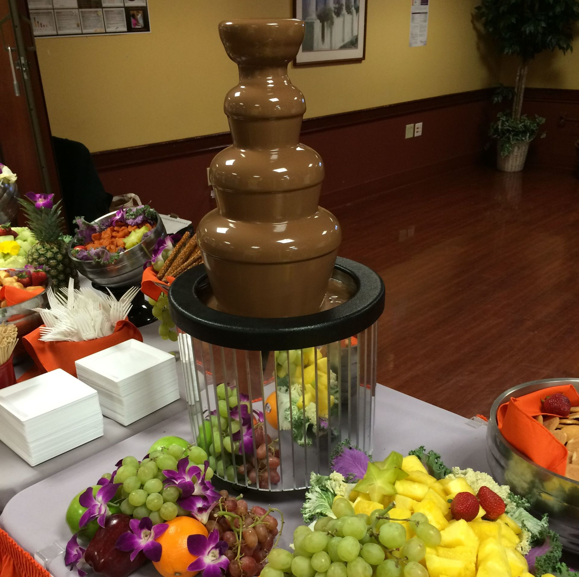 A chocolate fountain is surrounded by fruit on a table