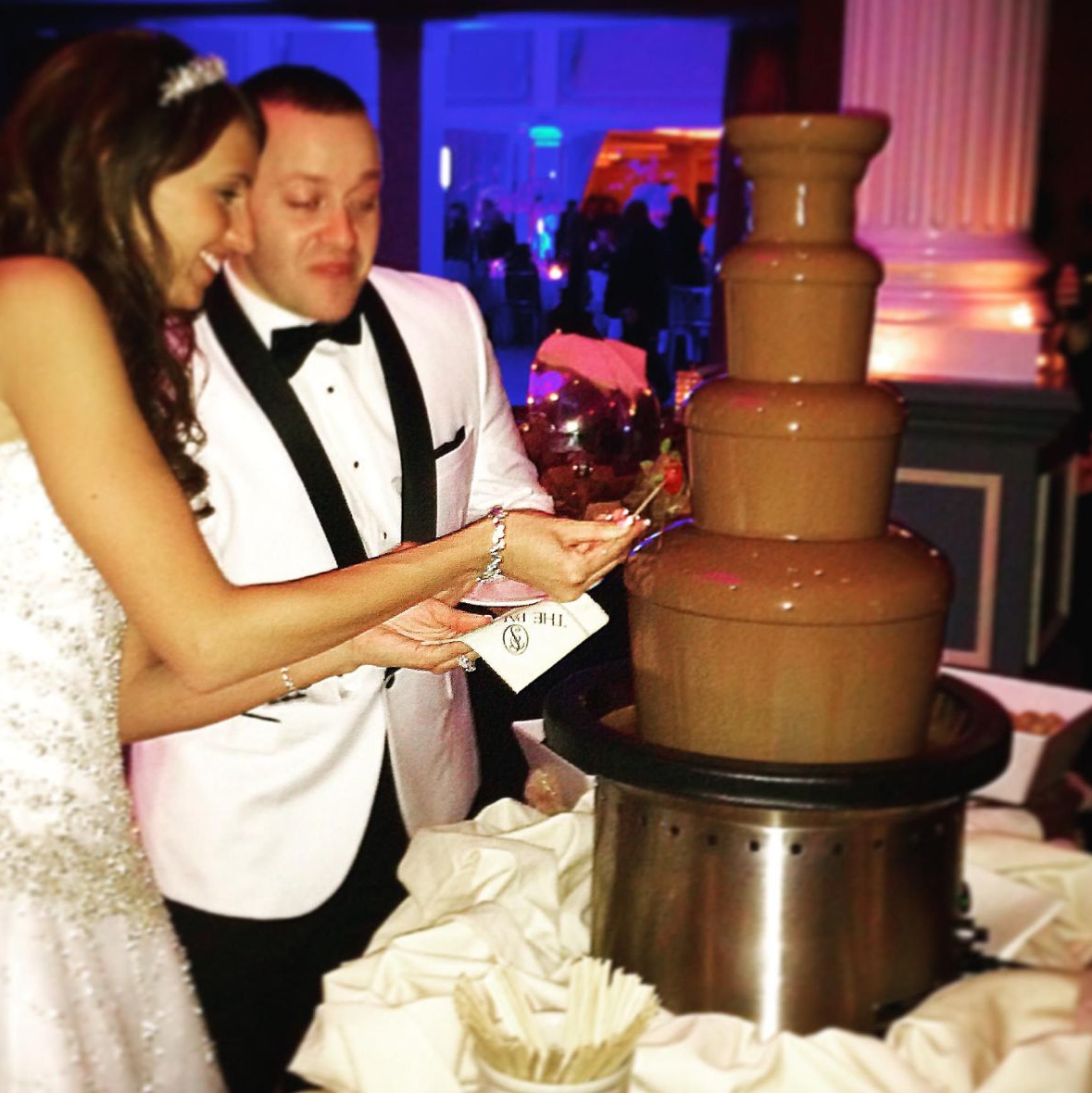 A bride and groom are standing in front of a chocolate fountain