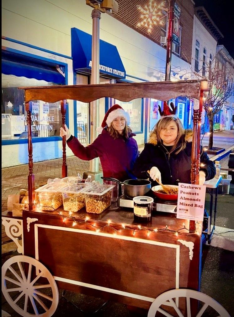 Two people standing behind a hot nut cart and preparing hot nuts for the holidays.