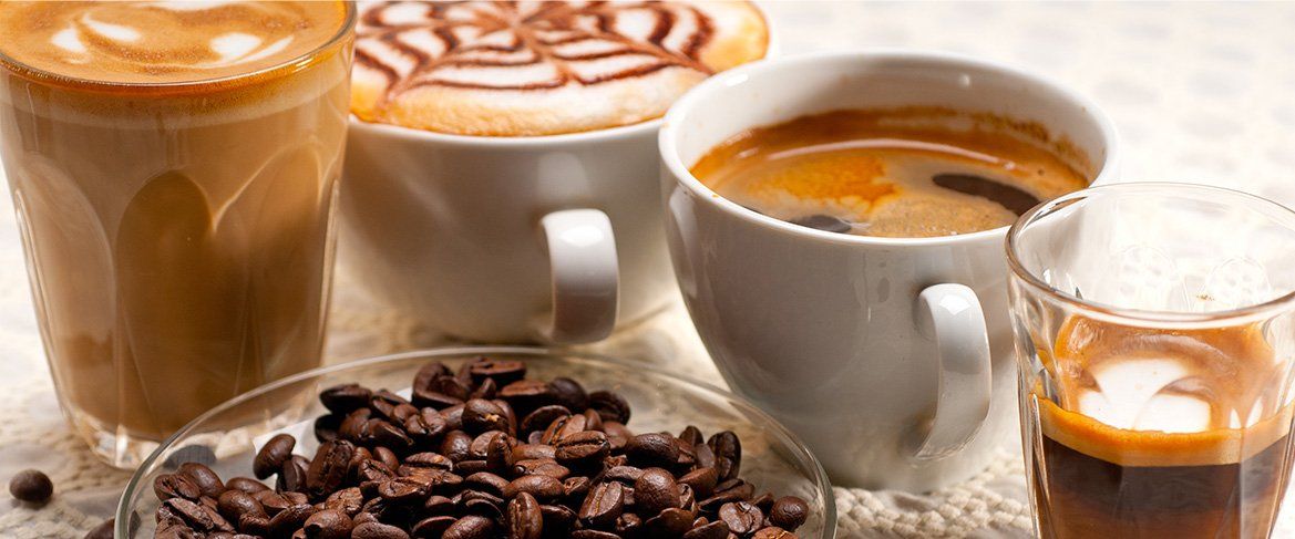 Four cups of coffee and a bowl of coffee beans on a table.