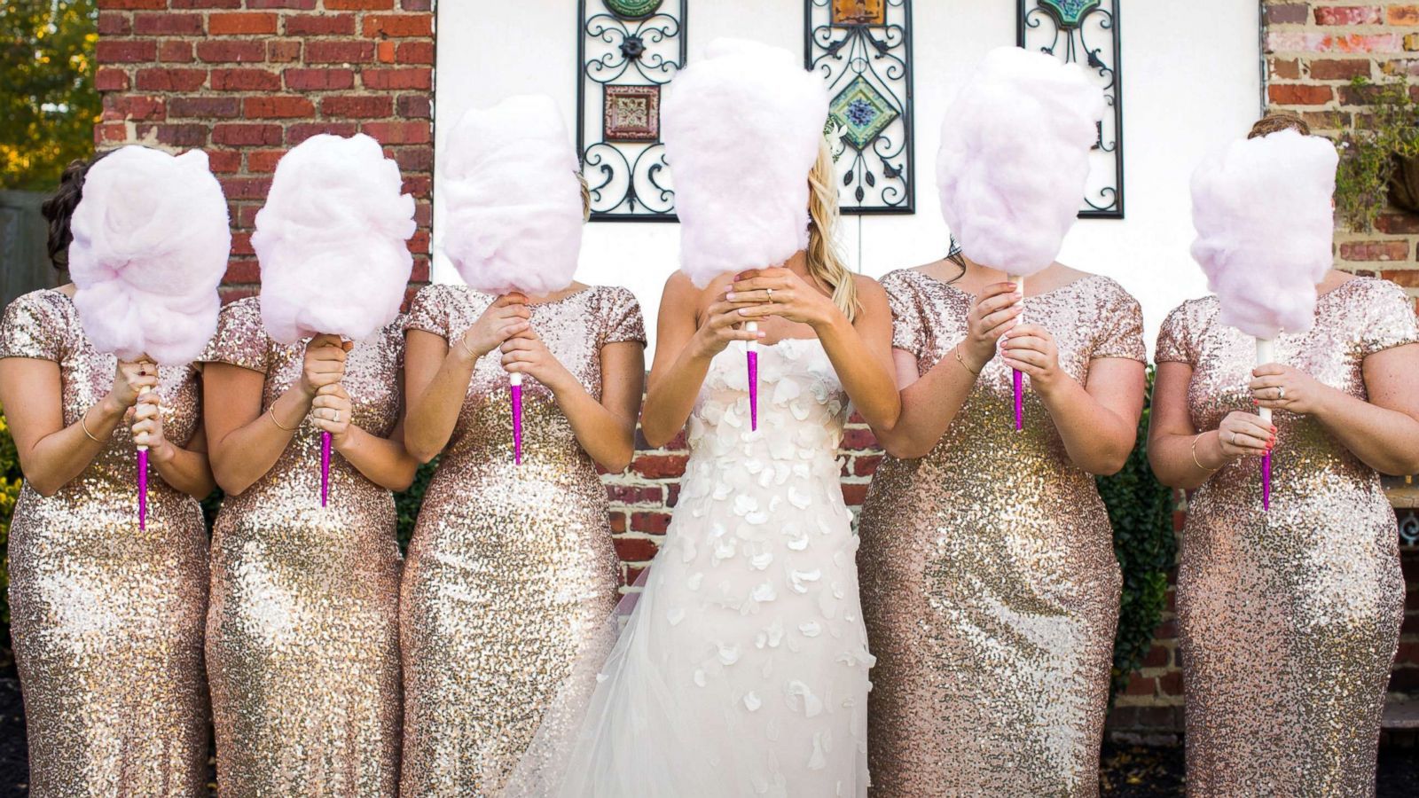 A bride and her bridesmaids are holding cotton candy in front of their faces.
