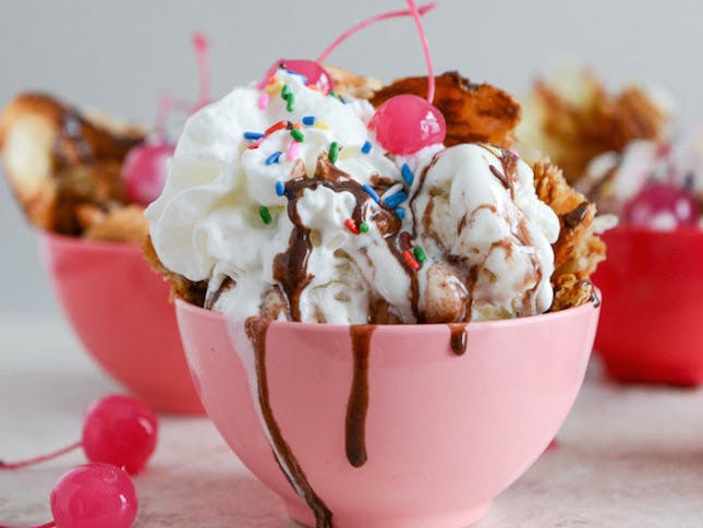 A bowl of ice cream with whipped cream , chocolate sauce and a cherry on top.