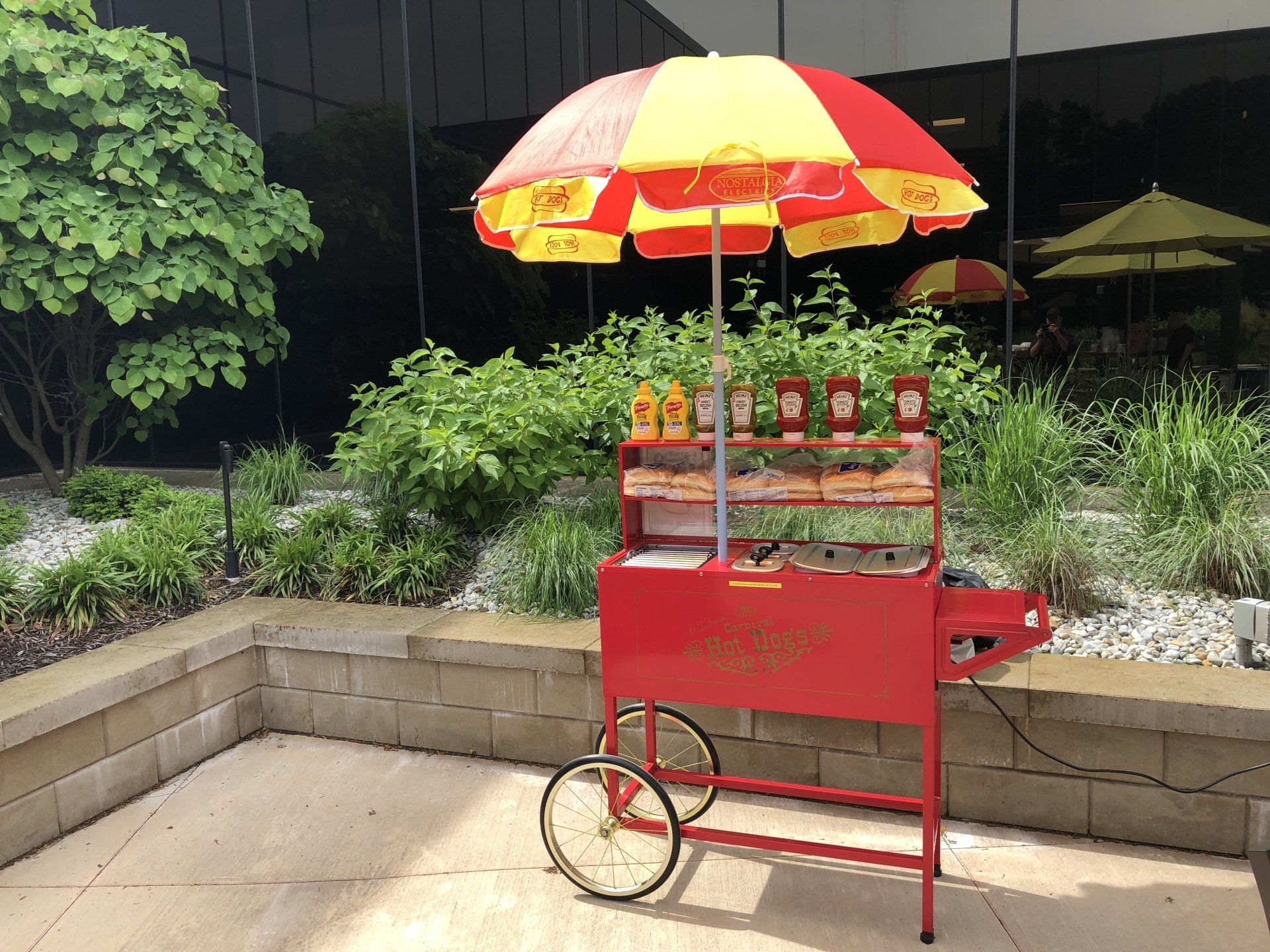 A red cart with a yellow and red umbrella on top of it.