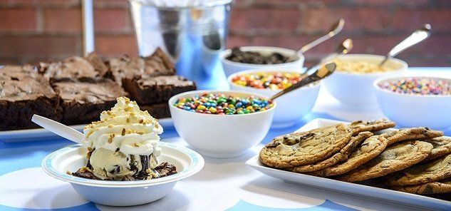 A table topped with bowls of ice cream , cookies , brownies and sprinkles.