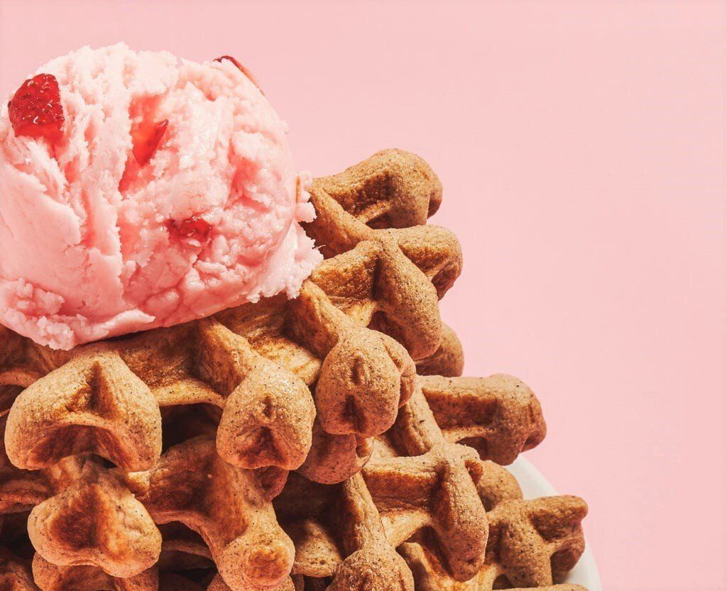 A stack of waffles with a scoop of strawberry ice cream on top.