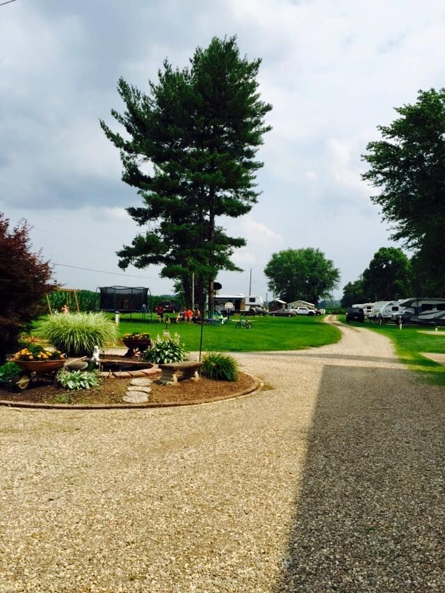 A gravel path leads toward a grassy lawn with a large pine tree, a small garden bed, and several parked RVs.