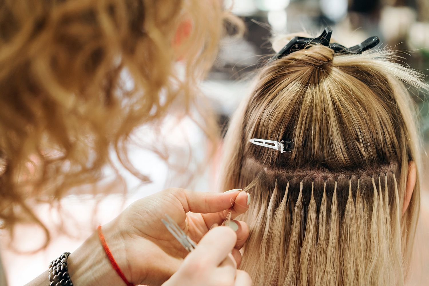 A woman is getting her hair extensions done by a hairdresser.