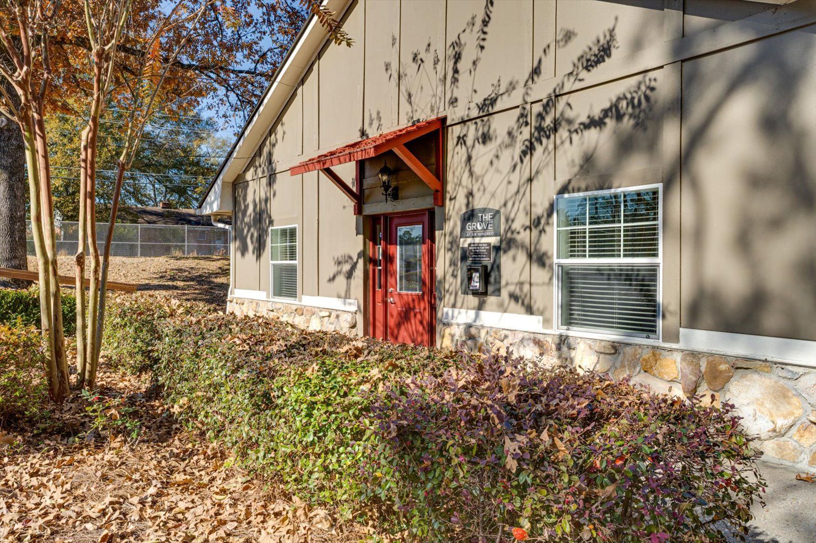 Building exterior with red door and windows, surrounded by autumn shrubs and trees