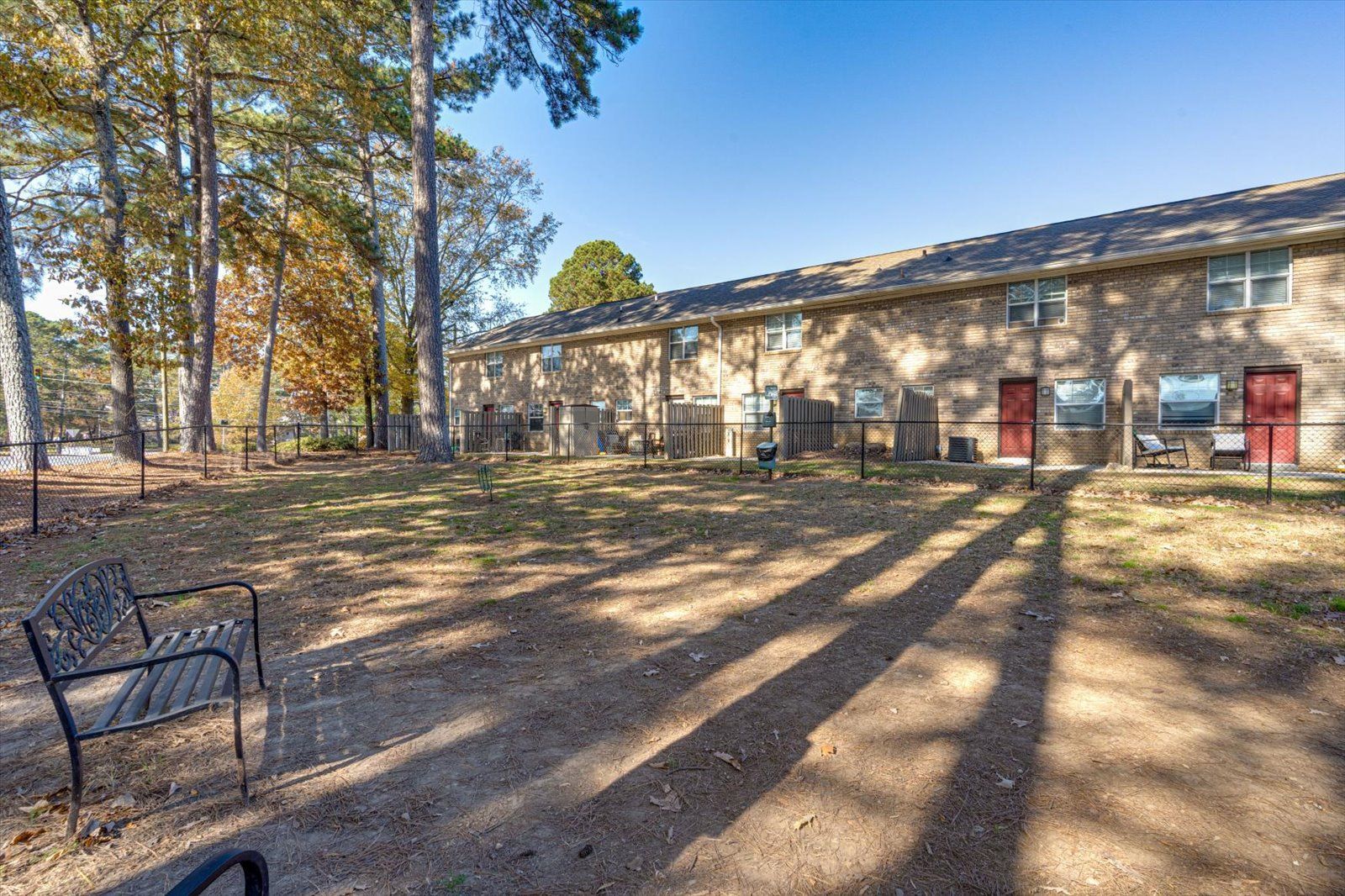 Brick apartment building with red doors, trees, and a bench in a sunlit courtyard